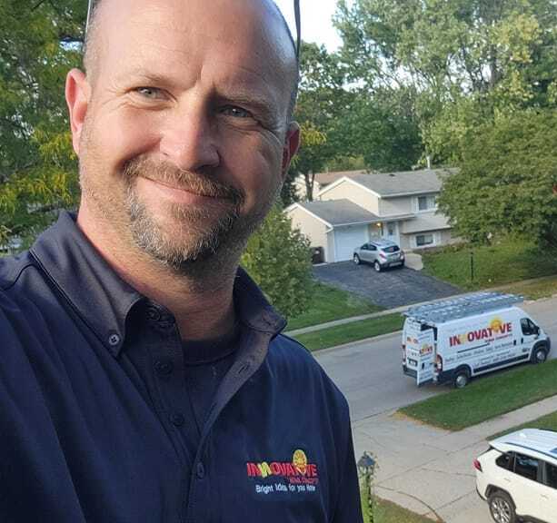 Man smiling in front of a residential neighborhood with company van in background.