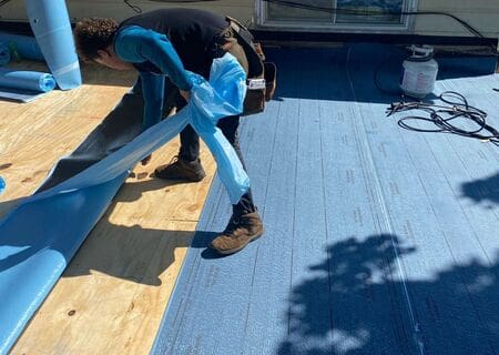IHC crew installing peel and stick membrane on a flat commercial roof