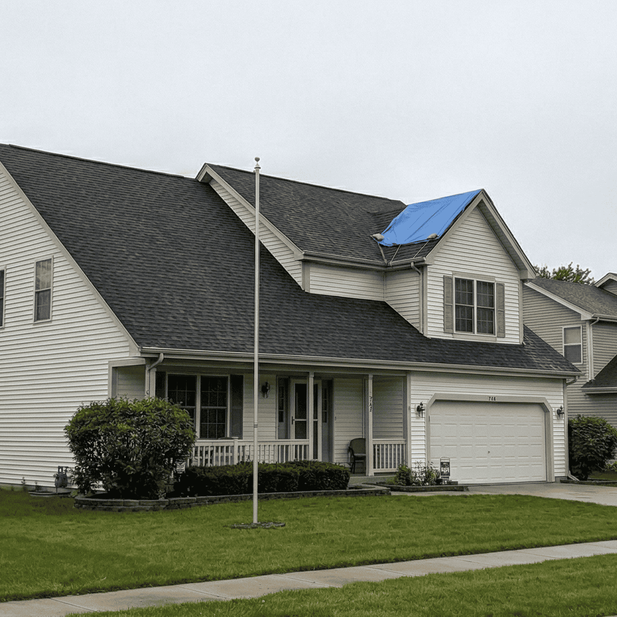Blue emergency tarp covering storm damage on a residential roof