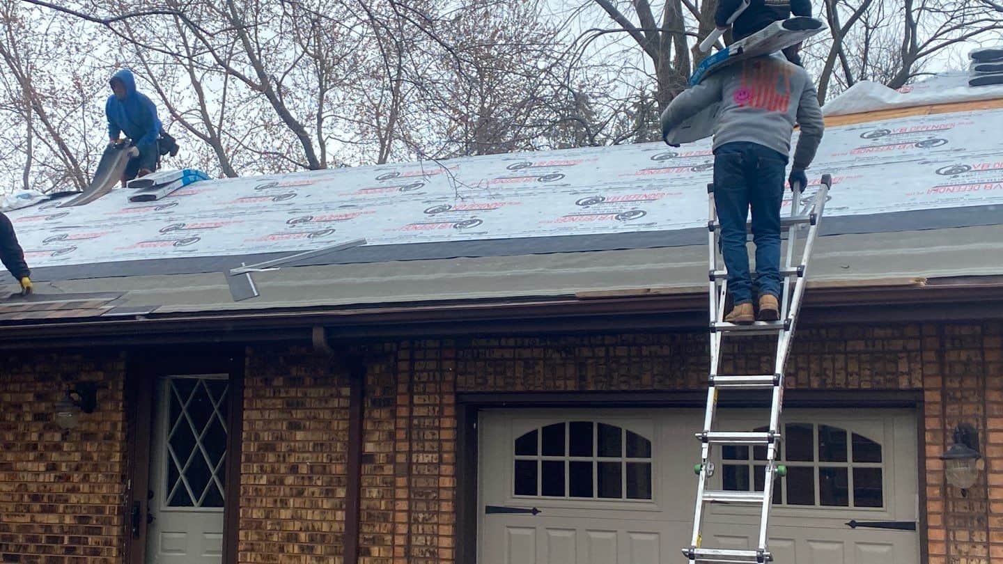 Roofer carrying a bundle of shingles up a ladder during a roof installation