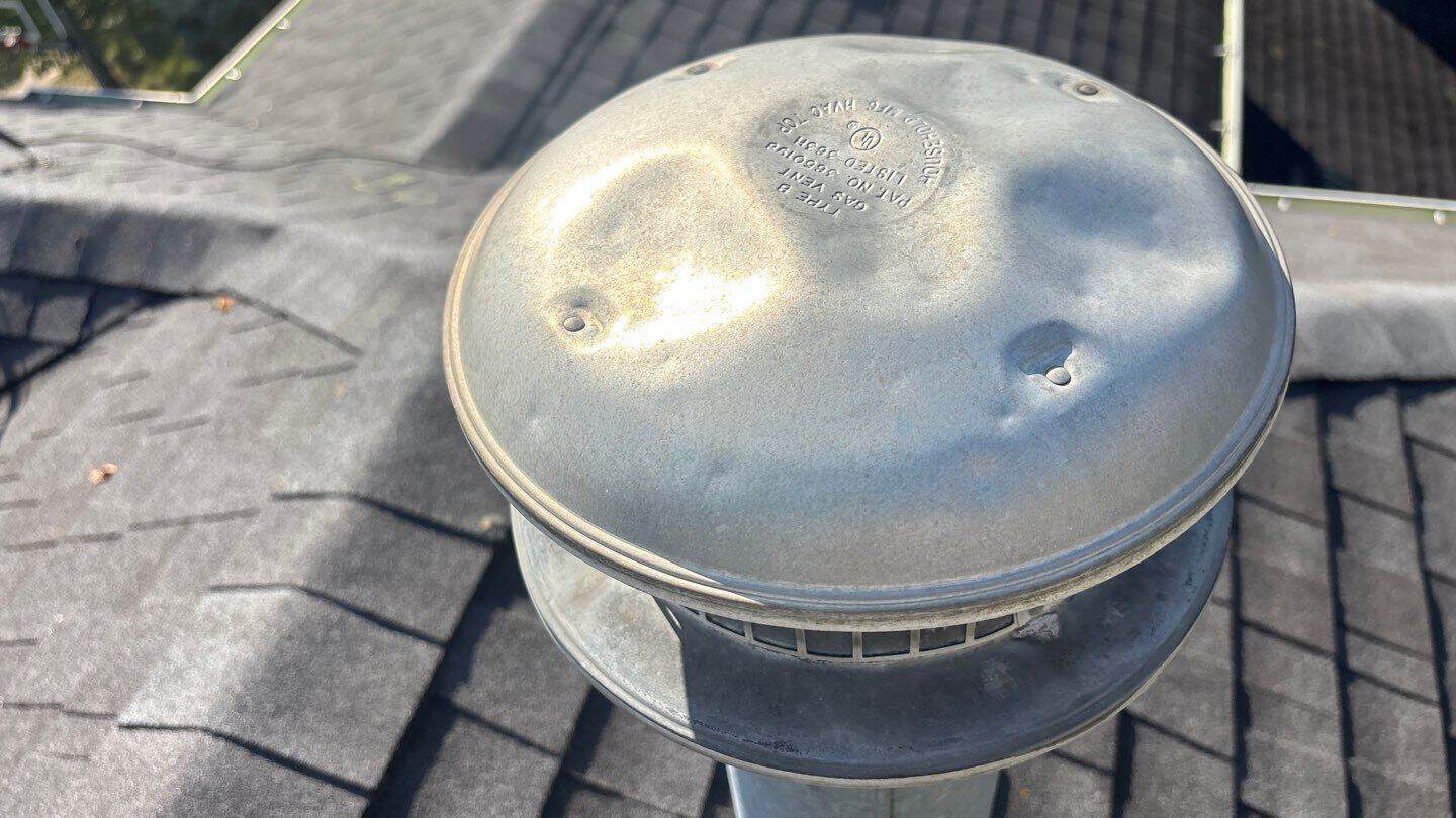 Hail-dented galvanized HVAC vent cap on a Cary, IL asphalt shingle roof after the August 2025 storm &mdash; soft metal shows impact when shingles look fine